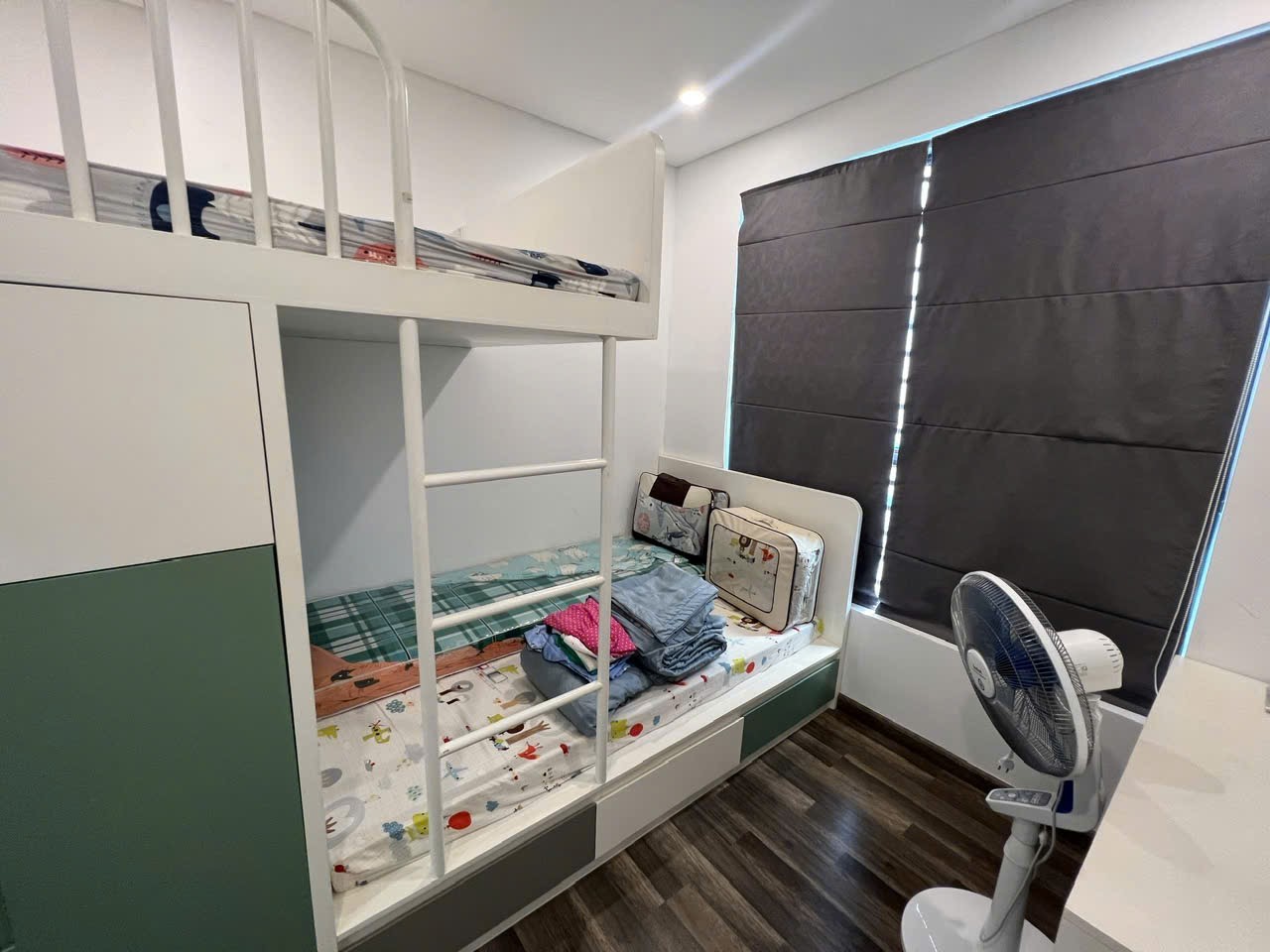 Phòng khách có sofa xanh, bàn trà, tivi và cửa kính căn hộ Jasmine 1